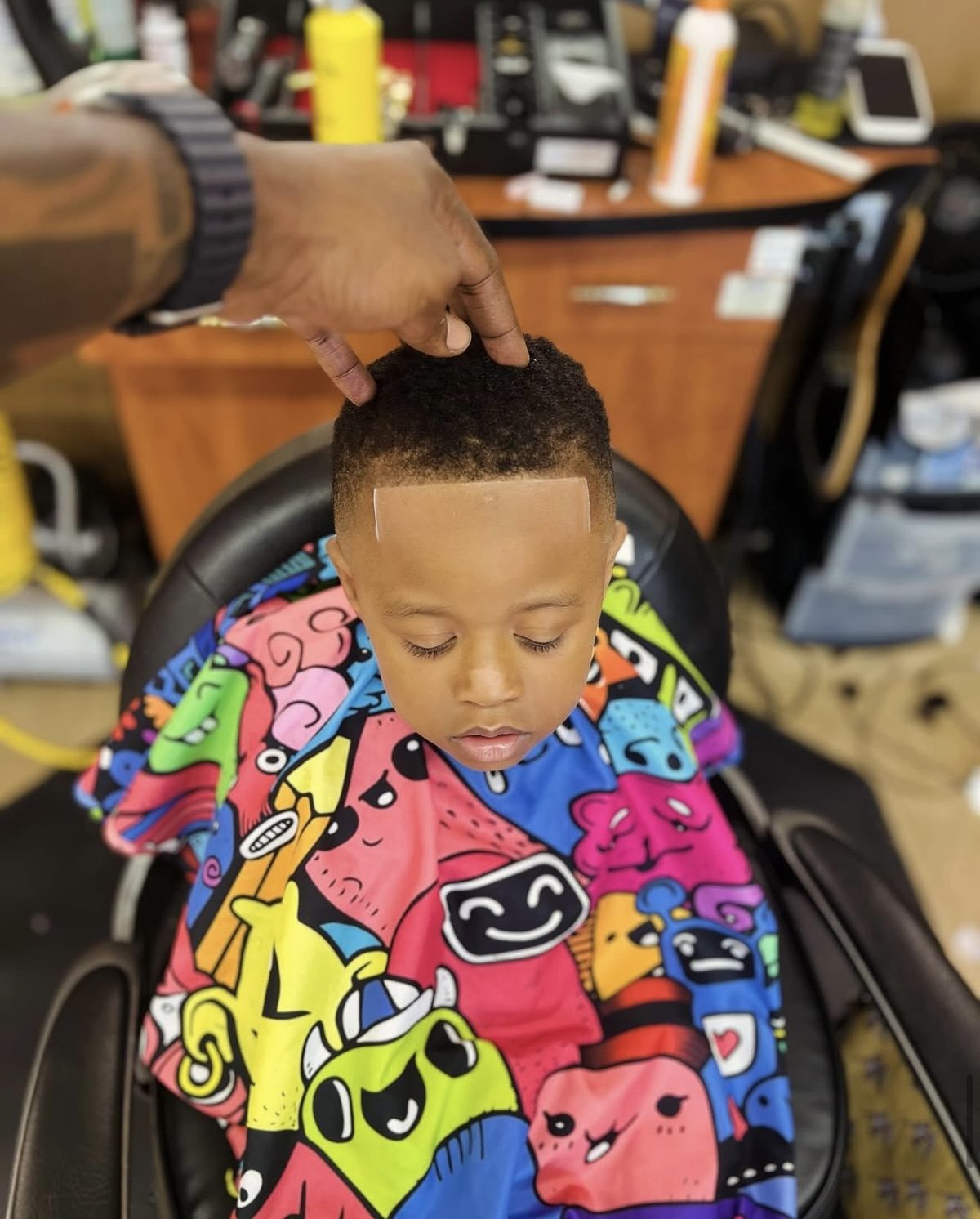 Young client with a fresh lineup in a colorful cape at Headlines Barbershop